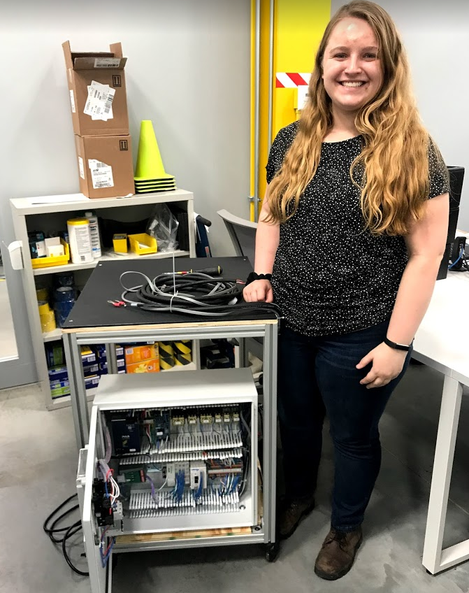 Intern Hannah standing next to some of her work from her summer internship.